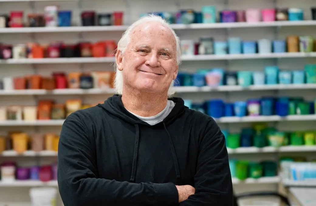 Rex Lamb, arms folded and smiling, in front of the shop's shelves of colored ink